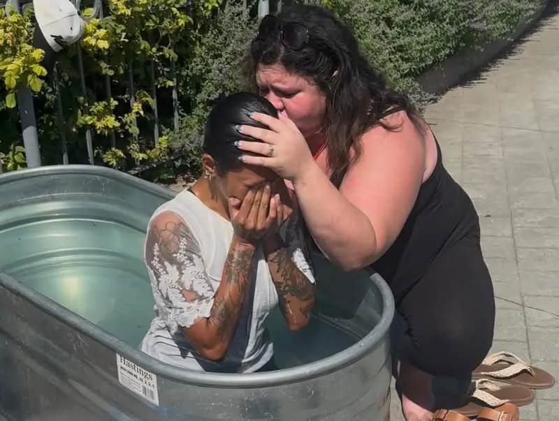 A woman embraces a man as he is baptized in a water tank at Jesus Festival Hamilton 2026